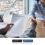 A candidate holds an employment contract while shaking hands with a recruiter, symbolizing a successful staffing partnership.