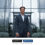 Professional in business attire stands alone in front of a glass building, representing talent in a competitive market