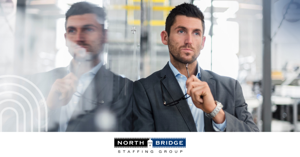 A professional leans on his reflection on a glass wall, symbolizing career transitions