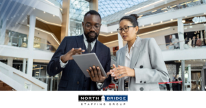 Two professionals stand discussing with a mobile tablet, symbolizing a recruiter helping a candidate evaluate a job offer strategically