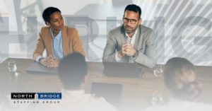 Four professionals in a business meeting at a conference table discussing hiring delays