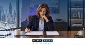 A professional woman writes in a planner at her desk in an office overlooking a city skyline. North Bridge Staffing Group logo.